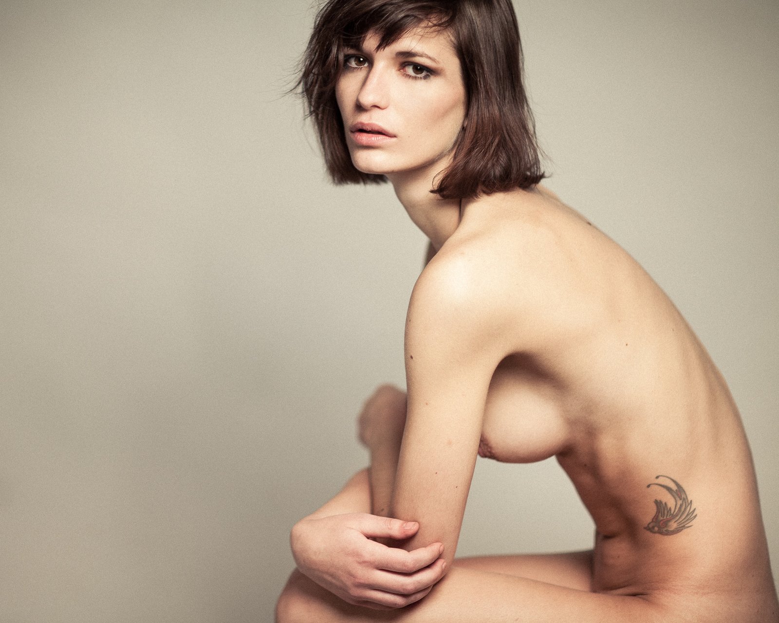Nu assis, bras croisés sur les genoux, tatouage