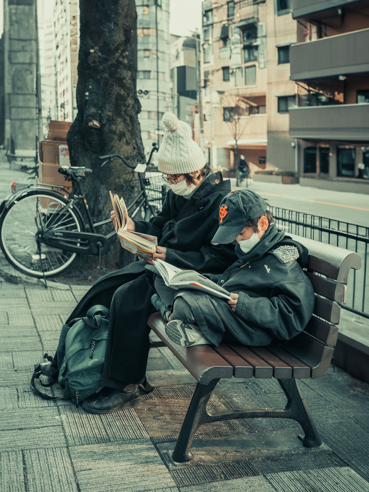 Mère et fils lisant un livre sur un banc, rue urbaine