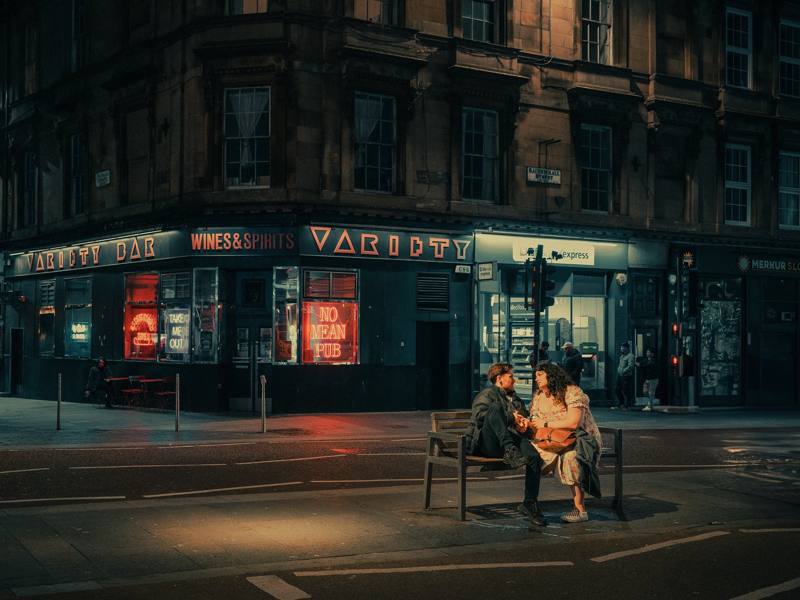 Couple assis sur un banc devant un bar néon la nuit