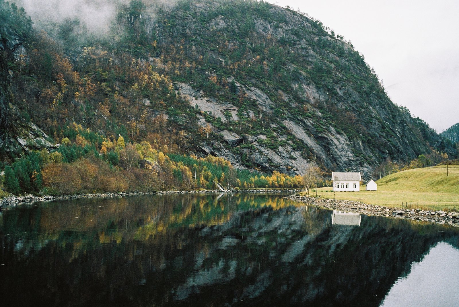 Maison blanche isolée au bord d'un fjord, montagne embrumée